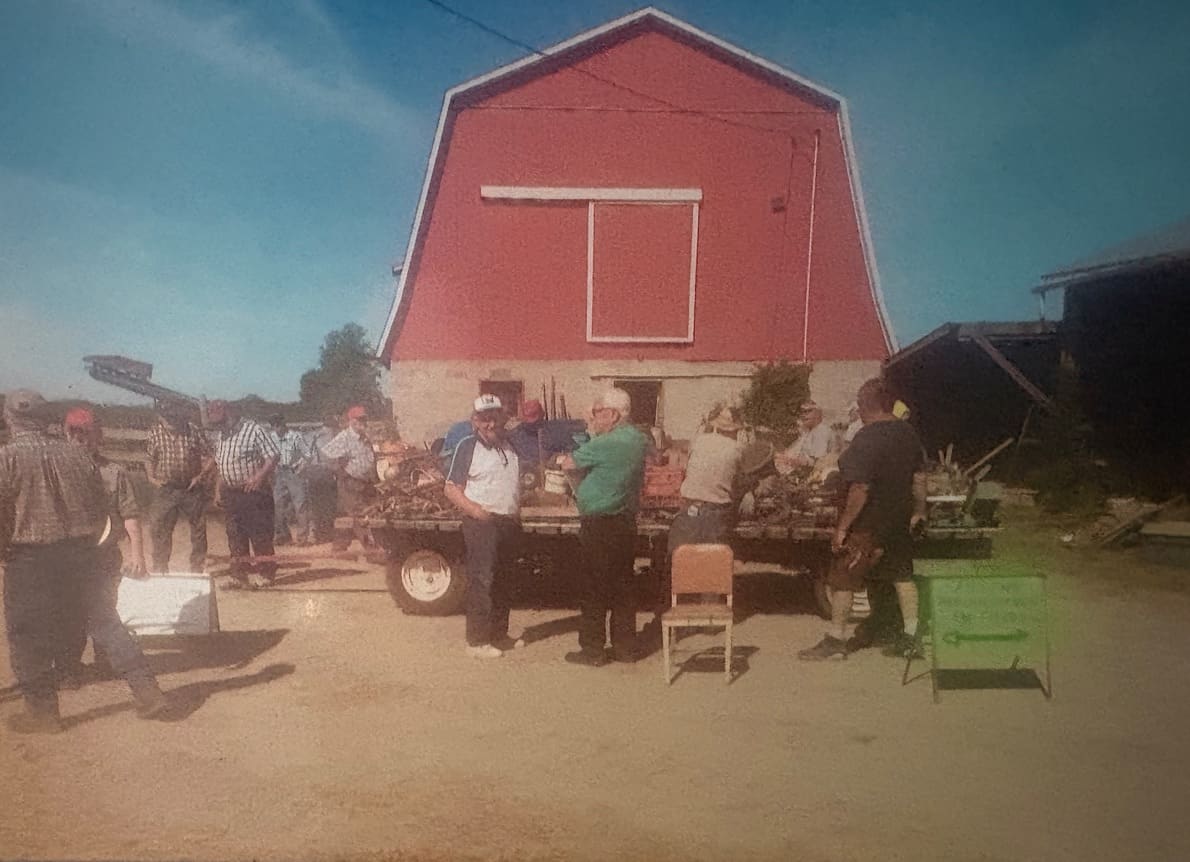 A crowd at an outdoor auction in front of a red barn (photograph from the JMAC Auctions website)