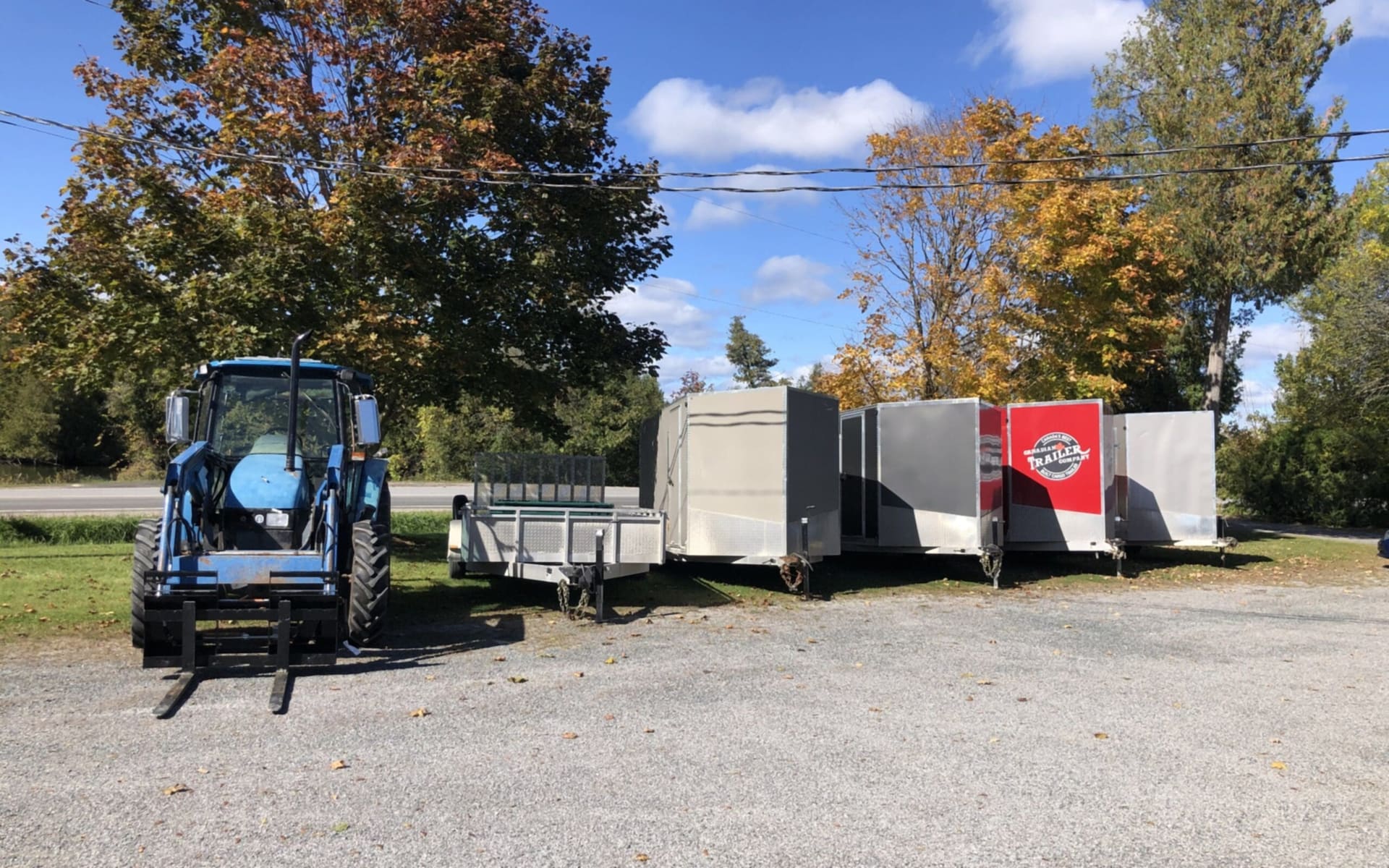 A tractor and enclosed trailers parked on a gravel lot in autumn (photograph from the JMAC Auctions website)