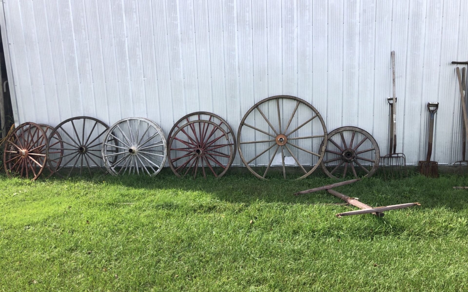 Antique wagon wheels and old farm tools against a steel building (photograph from the JMAC Auctions website)