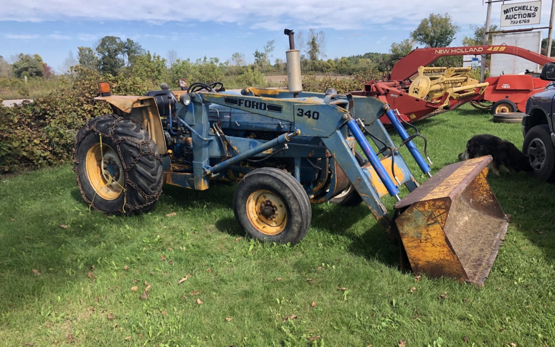 A Ford 340 loader tractor on the grass with hay equipment behind (photograph from the JMAC Auctions website)